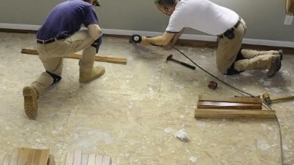 Two workers kneeling on a subfloor while removing damaged flooring